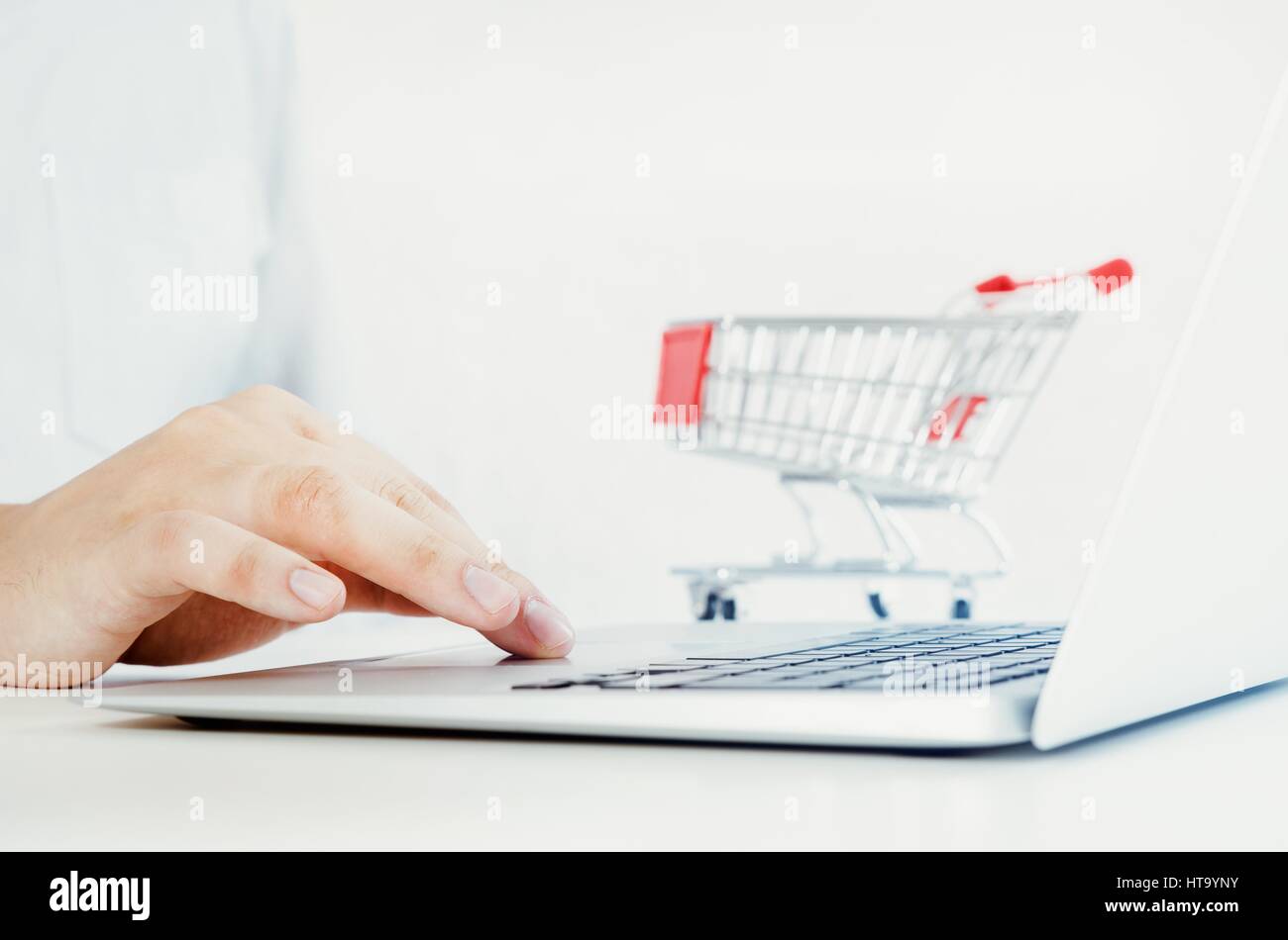 Man using laptop for internet shopping. Bright composition with shopping trolley in background. Stock Photo