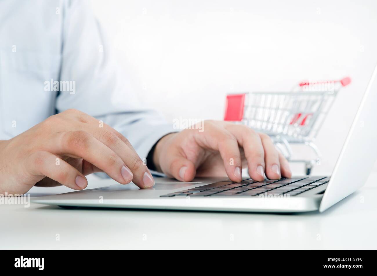 Man using laptop for internet shopping. Bright composition with shopping trolley in background. Stock Photo