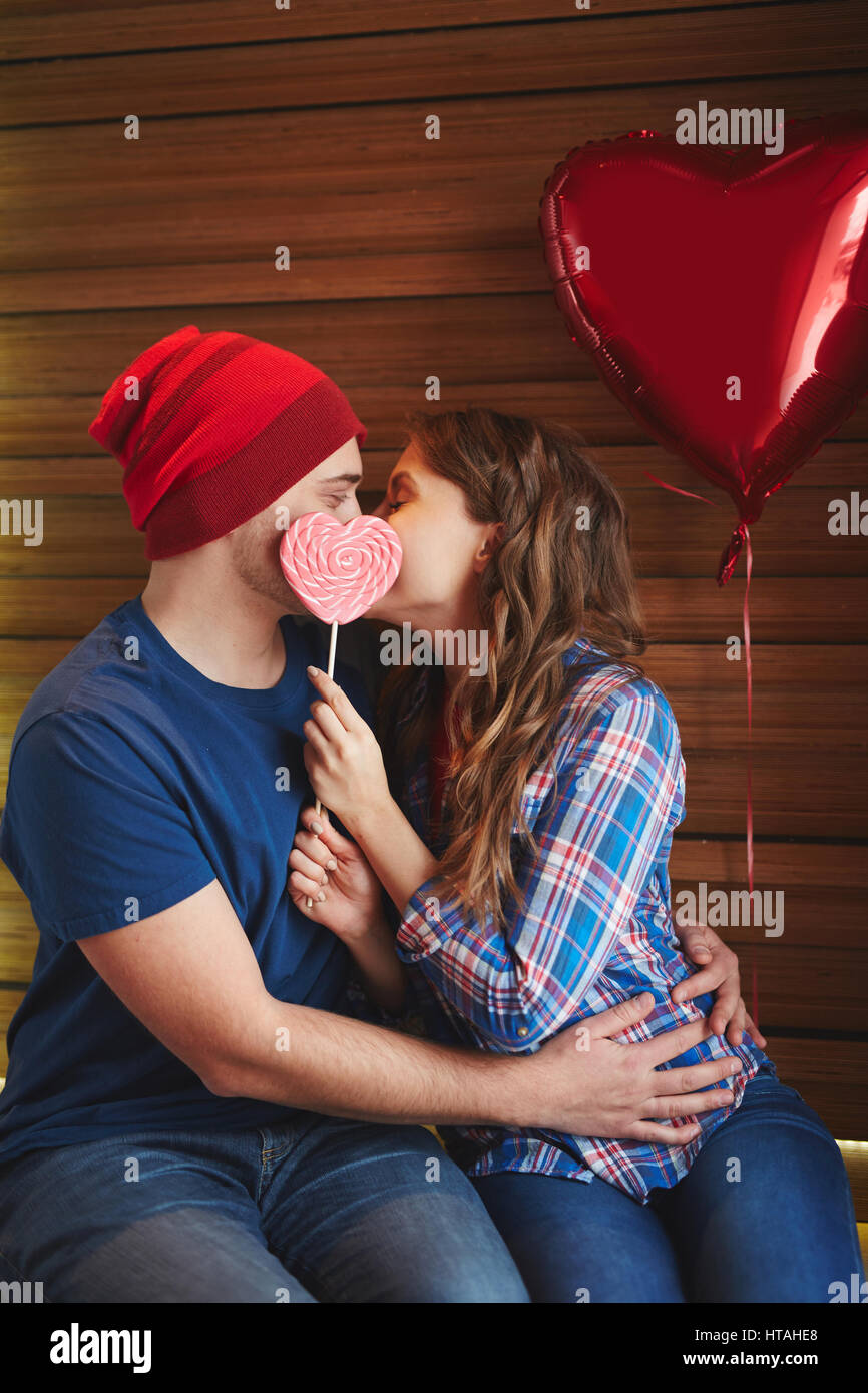 Amorous dates with heart-shaped candy and balloon kissing in embrace Stock Photo