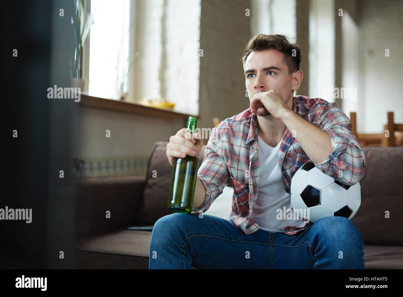 Nervous football fan with bottle of beer watching match on tv Stock Photo