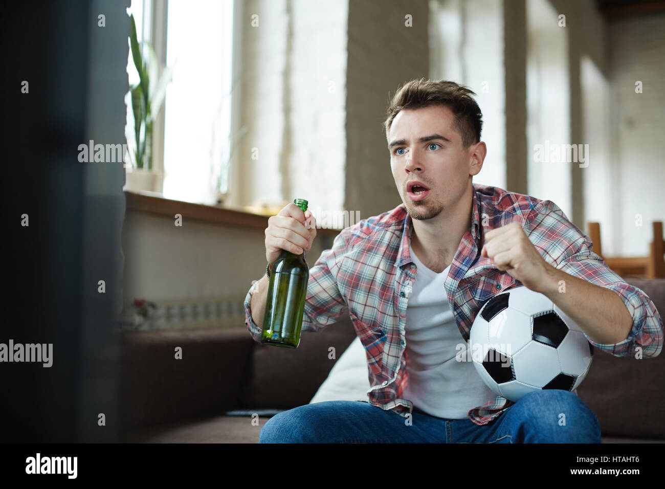 Man with ball and beer sitting in front of tv set Stock Photo