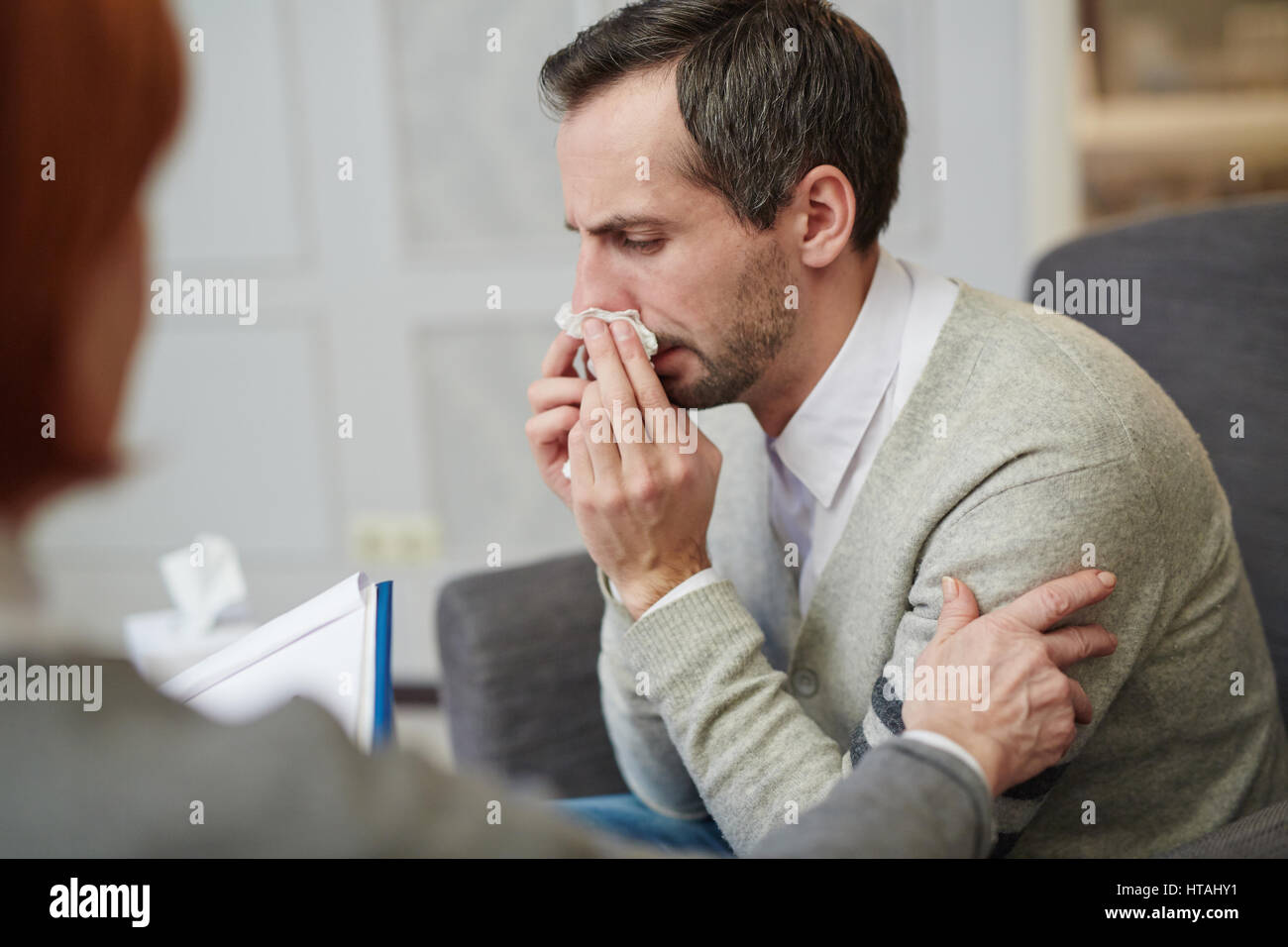 Crying man with handkerchief wiping tears while counselor reassuring him Stock Photo