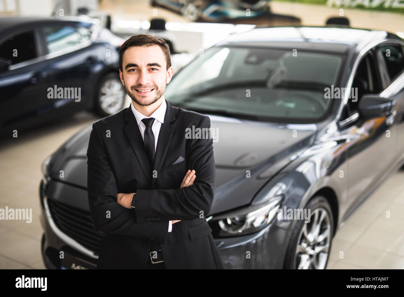 Handsome young classic car salesman standing at the dealership in front