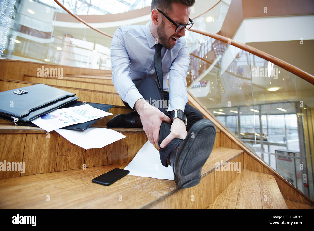 Businessman holds his injured leg on staircase and crying Stock Photo