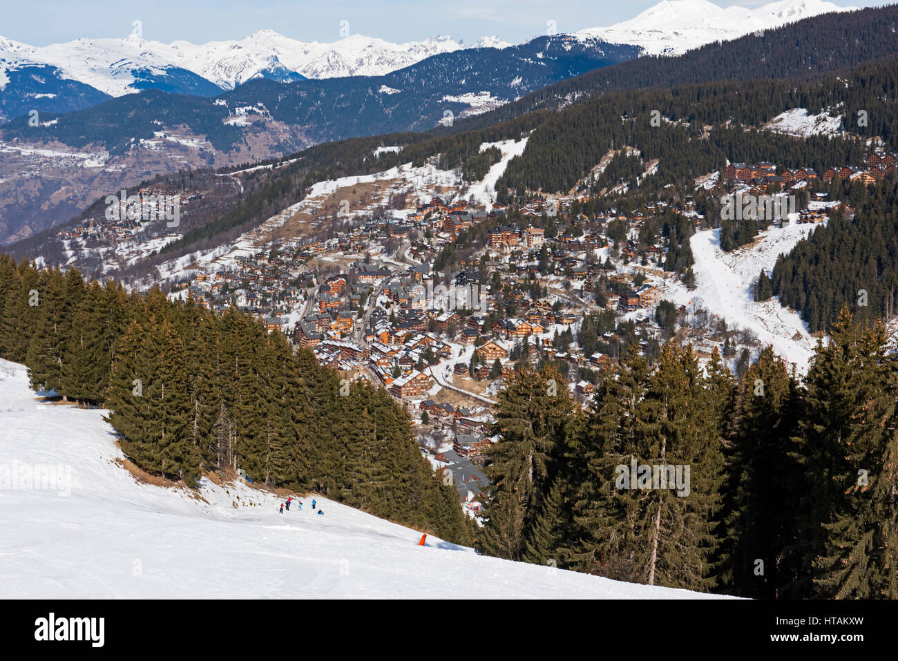 Panoramic view down snow covered valley in alpine mountain range with conifer pine trees and village Stock Photo