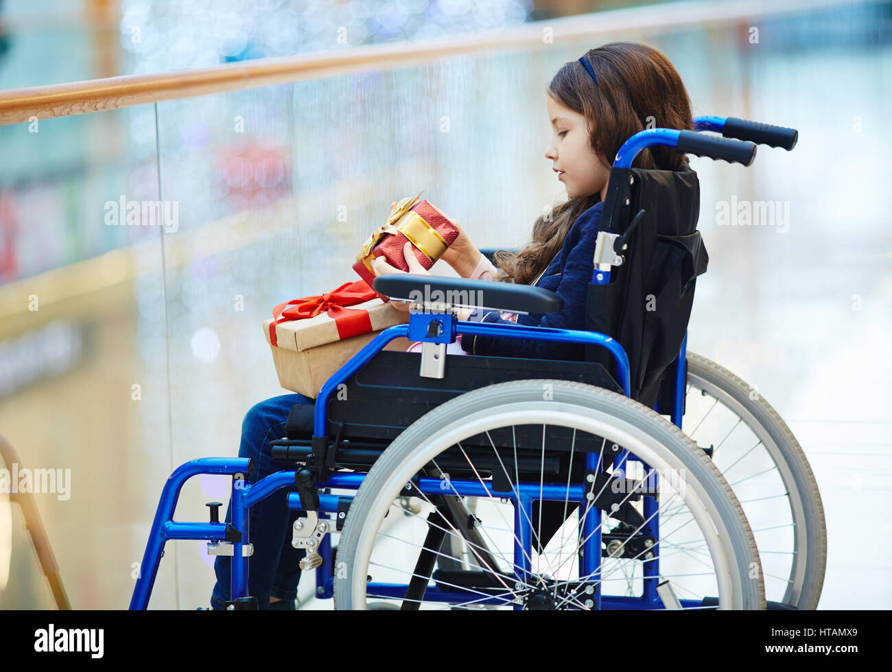 Sideview of disabled child in wheelchair looking at giftbox Stock