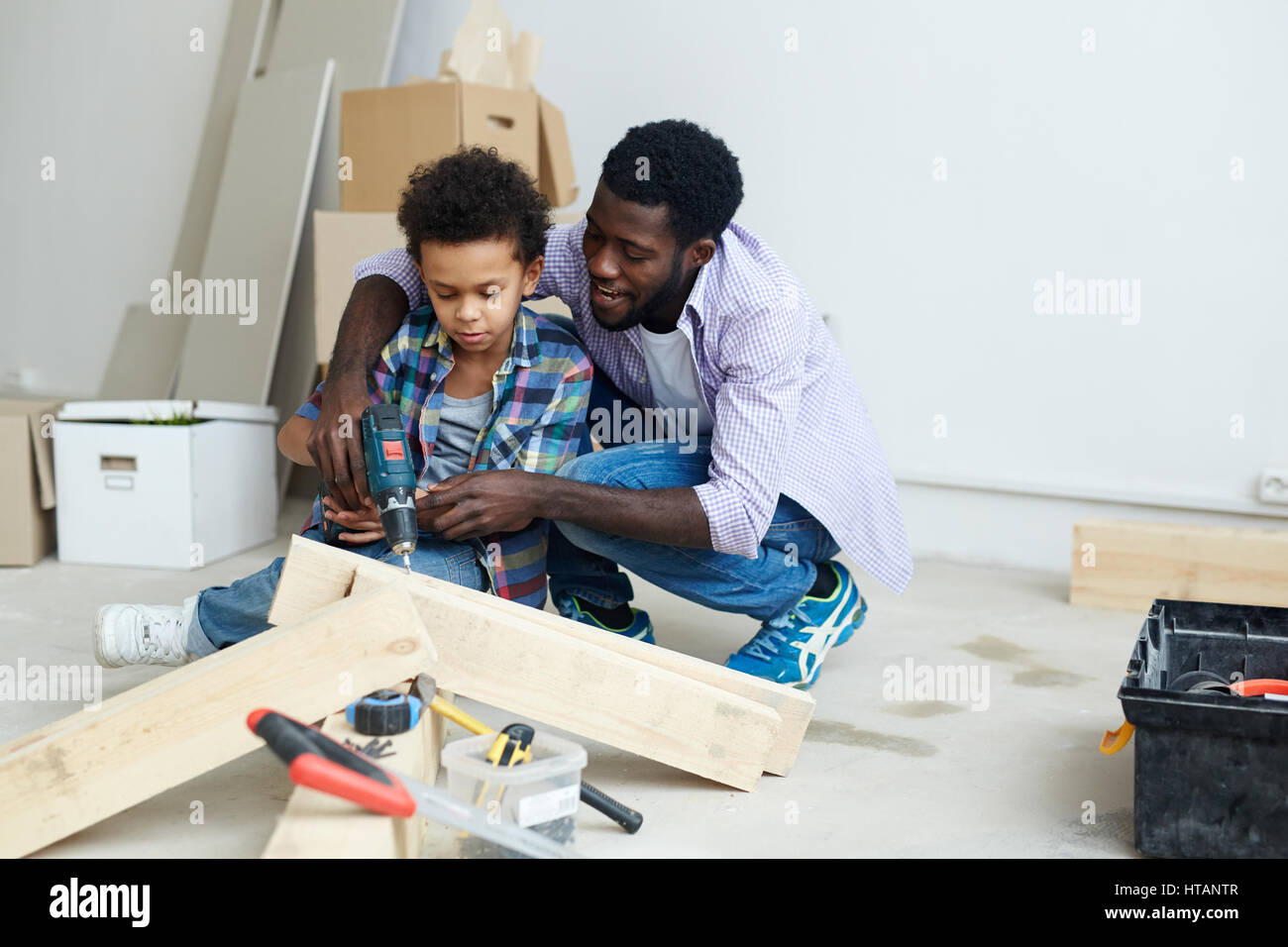 Young man and little boy drilling wooden plank Stock Photo - Alamy