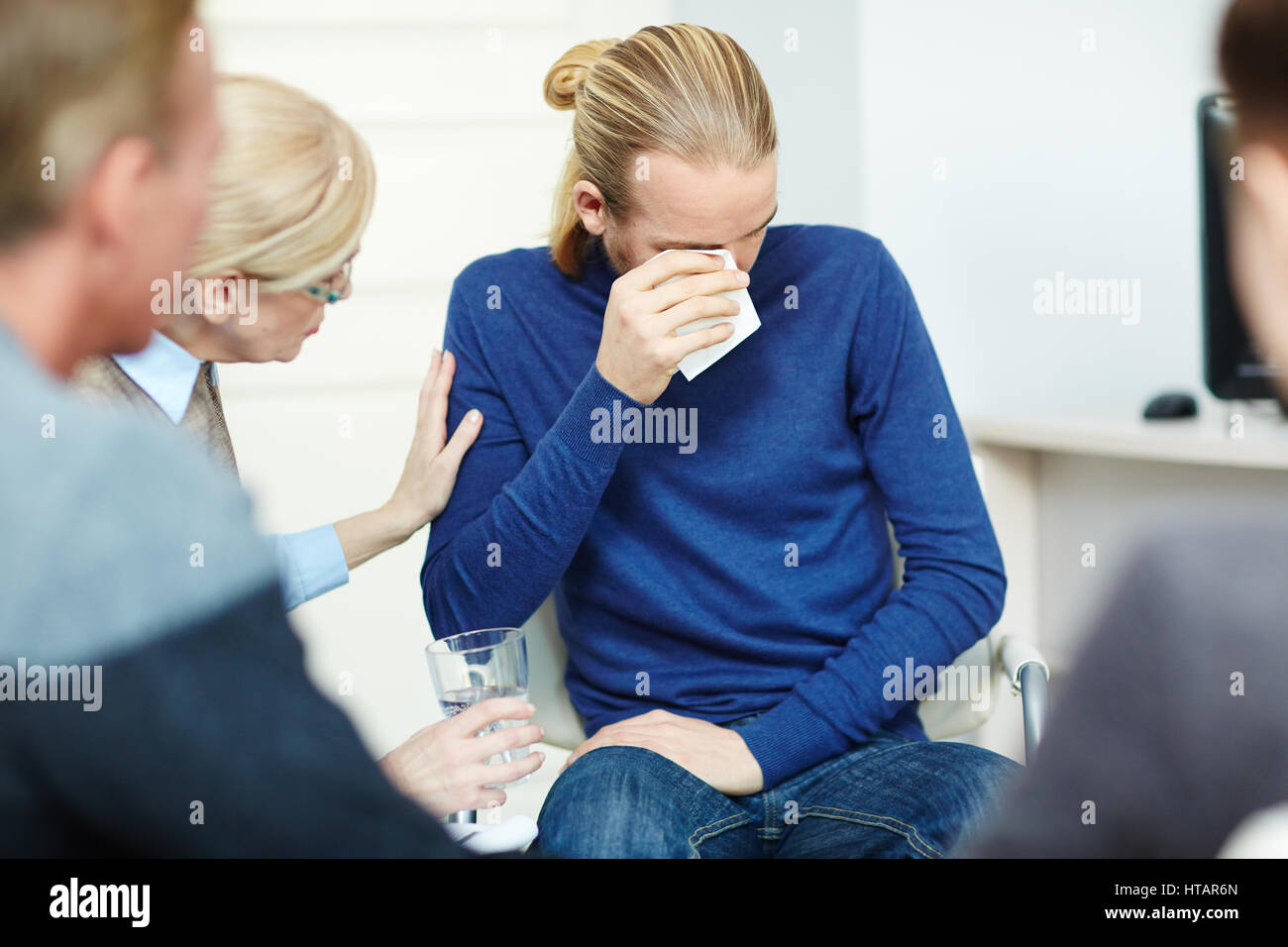 Portrait of young man sitting in circle of psychological support group crying while sharing his trouble with mentor and other participants Stock Photo