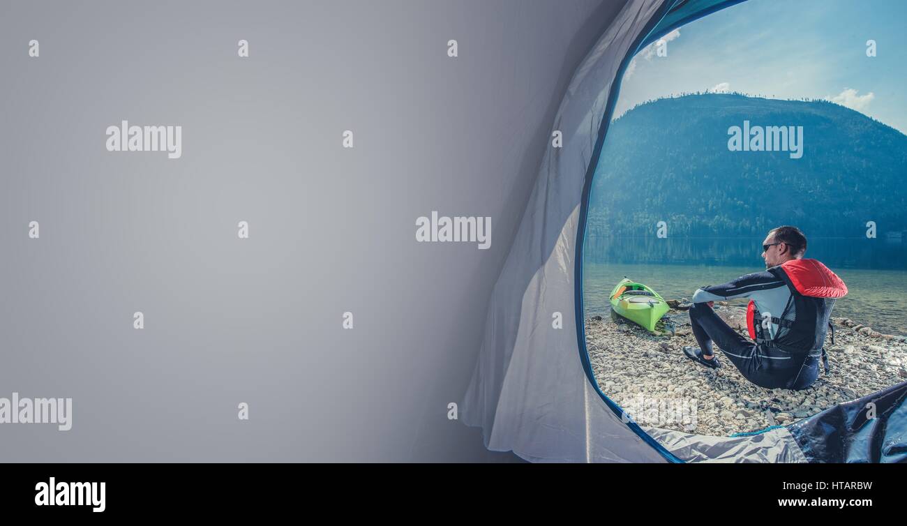 Scenic Lake Shore Camping with Kayak. Caucasian Sportsman in the Wetsuit Preparing For Kayak Trip. Photo with Copy Space. Stock Photo