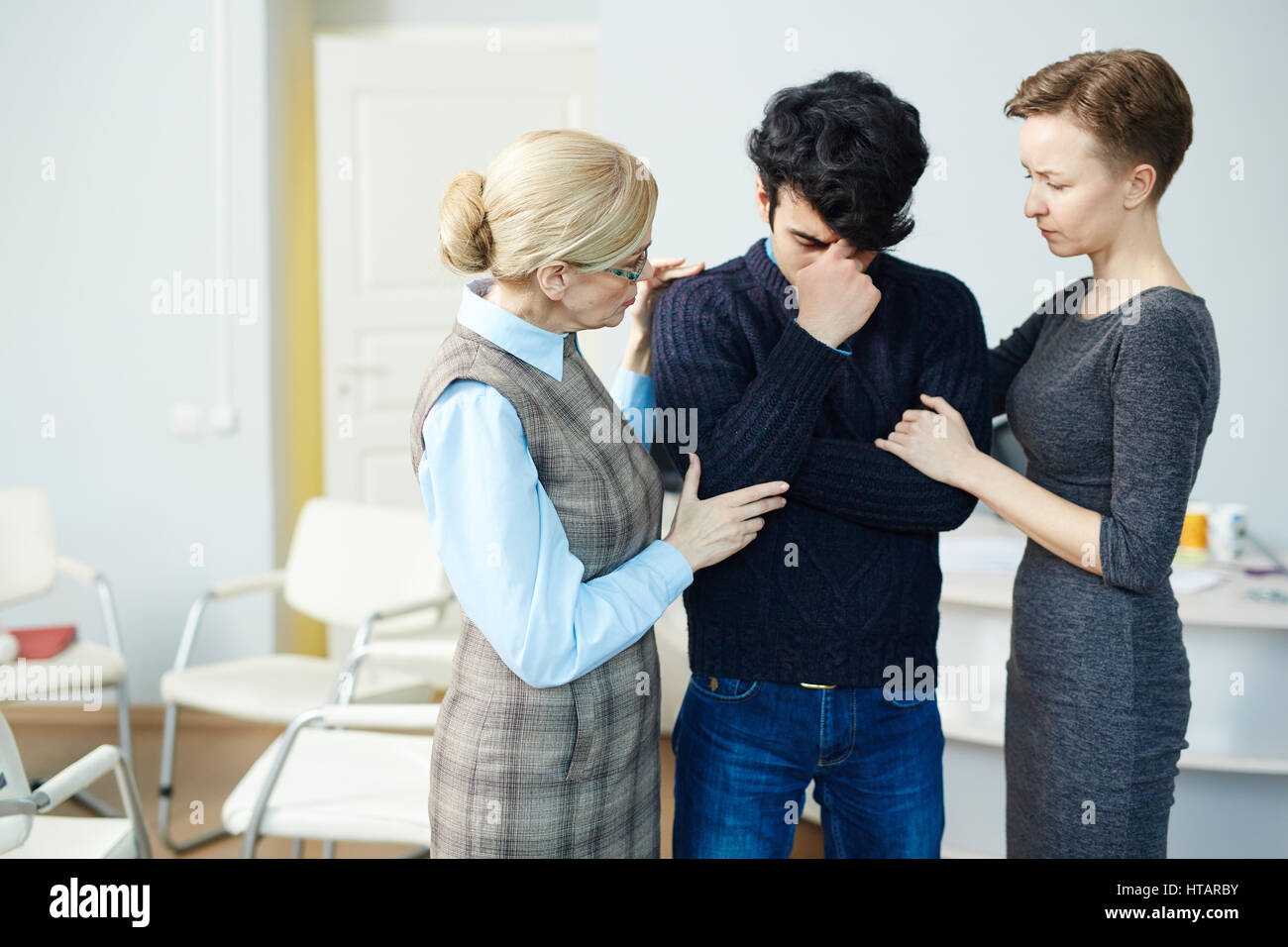 Portrait of mentor and wife comforting young crying man after psychological therapy session Stock Photo