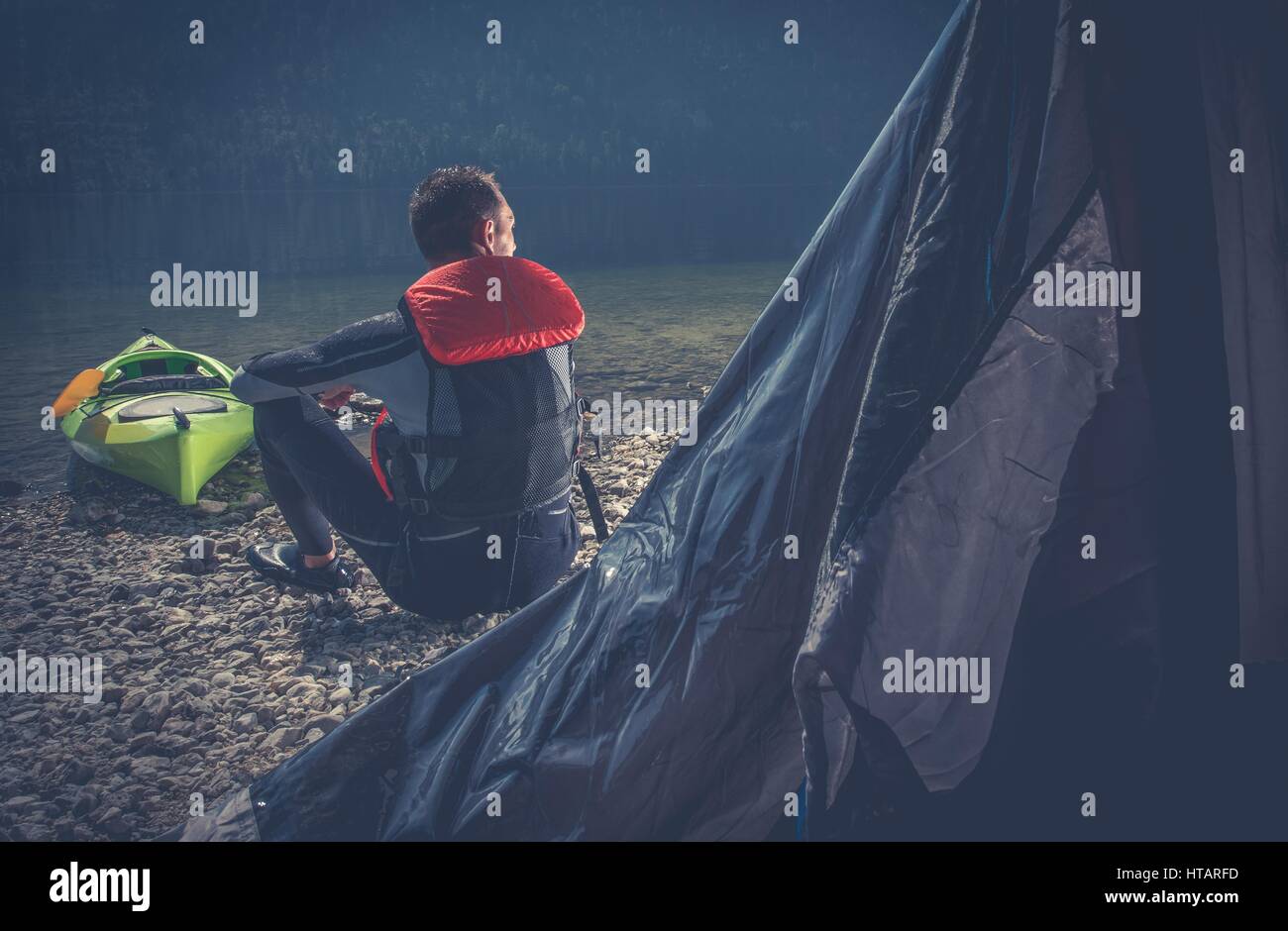 Outdoor Sportsman Camping. Caucasian Men in Wetsuit on the Camping on the Edge of Scenic Lake. Stock Photo