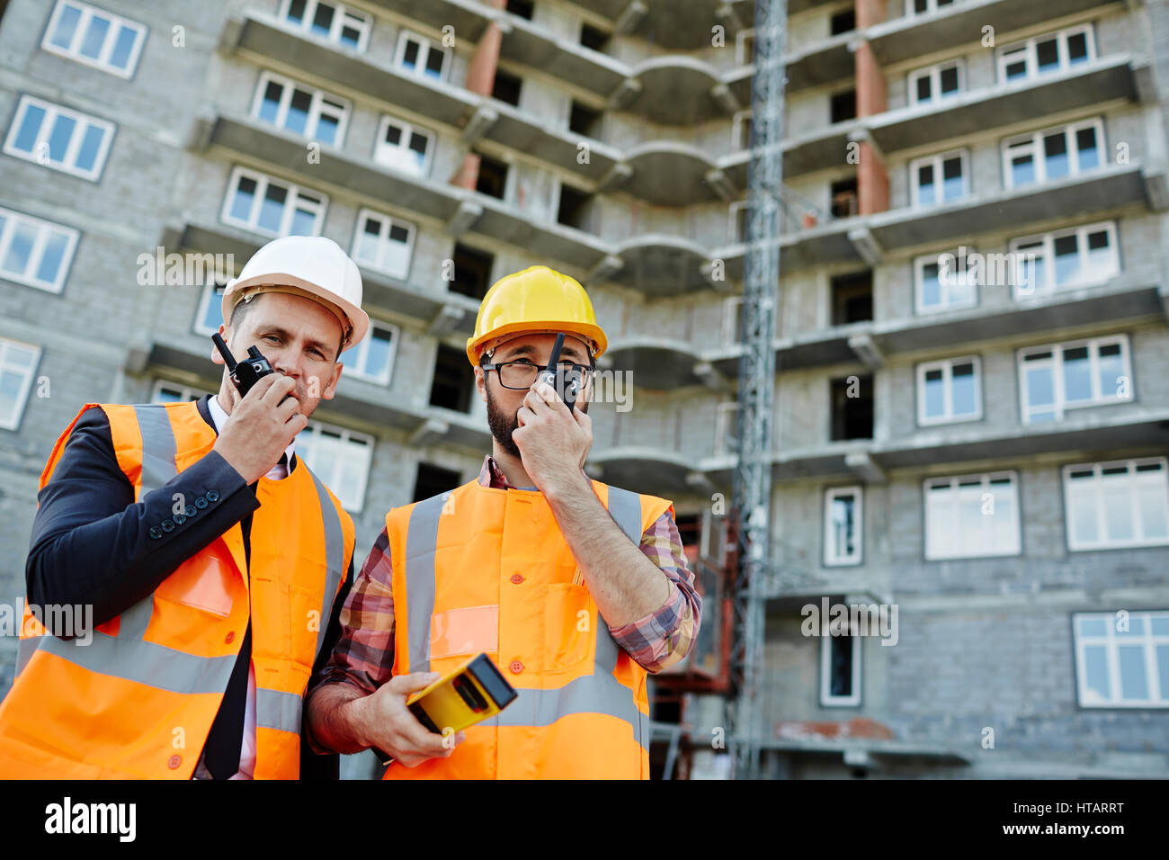 Portrait of two workmen wearing reflective orange vests and hard hats ...