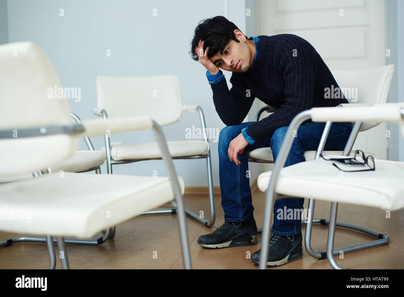 Adolescent man sitting on chair and touching his head Stock Photo
