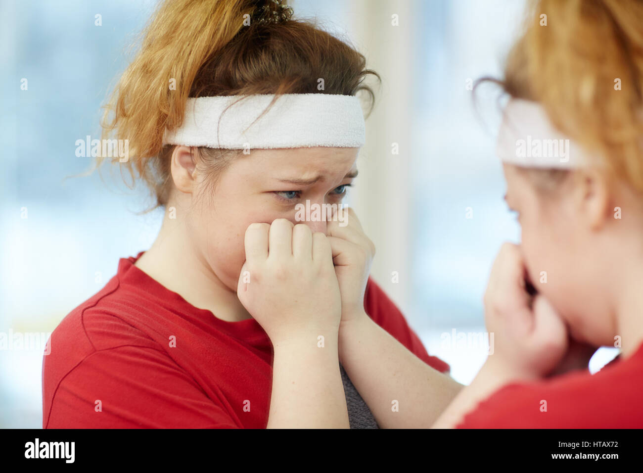 Portrait of young overweight woman crying while looking in mirror, upset and dissatisfied with her body image Stock Photo