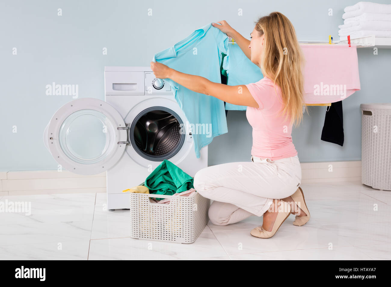Young Woman Looking At Clothes After Washing In Washing Machine At
