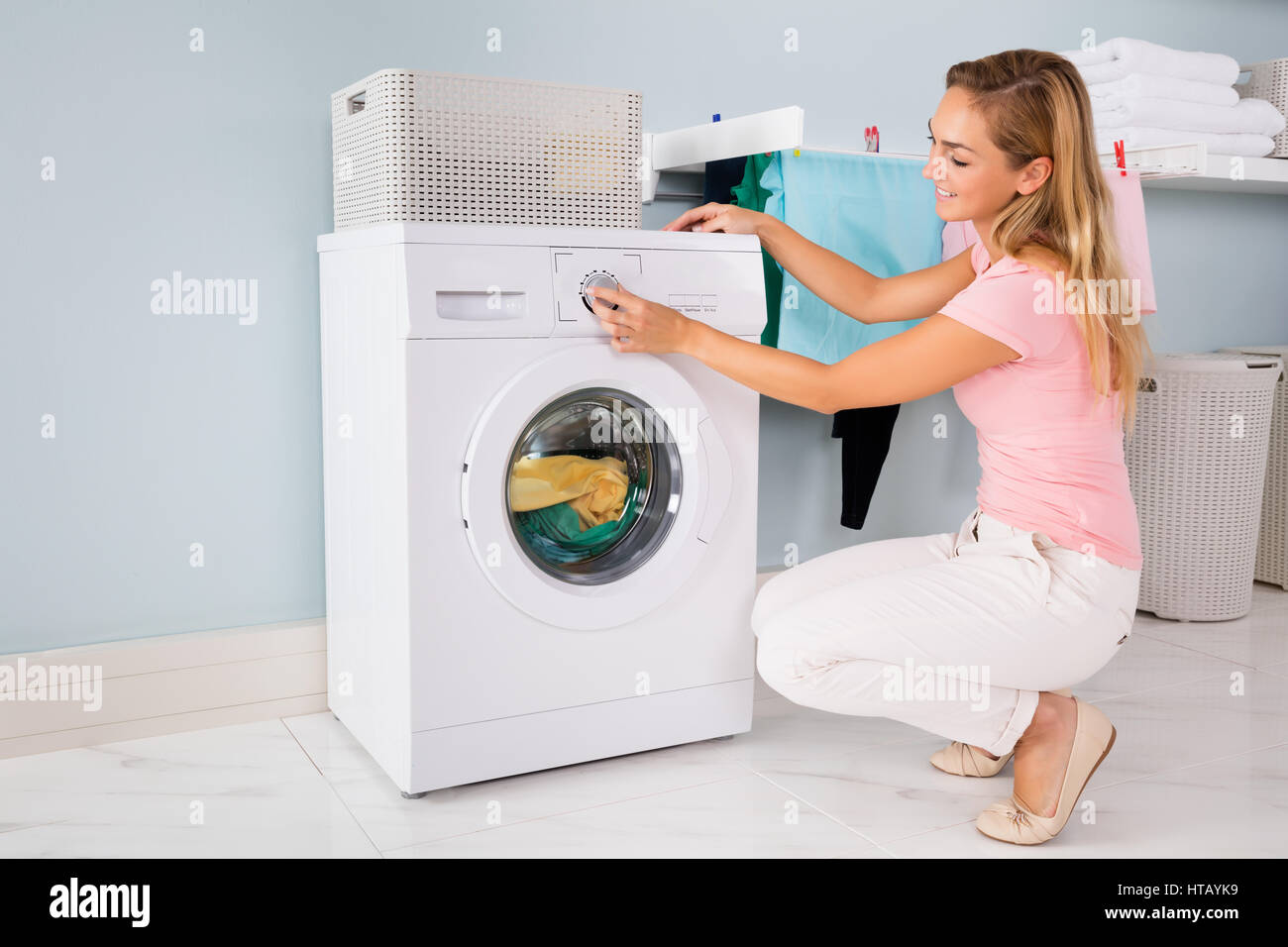 Young Smiling Woman Using Washing Machine To Clean Clothes In Laundry
