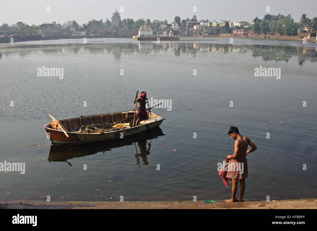 Cleaning up the lake 'bindu sagar' + young man ready to bathe in the lake ( India) In the background, the Lingaraj temple is visible. Stock Photo