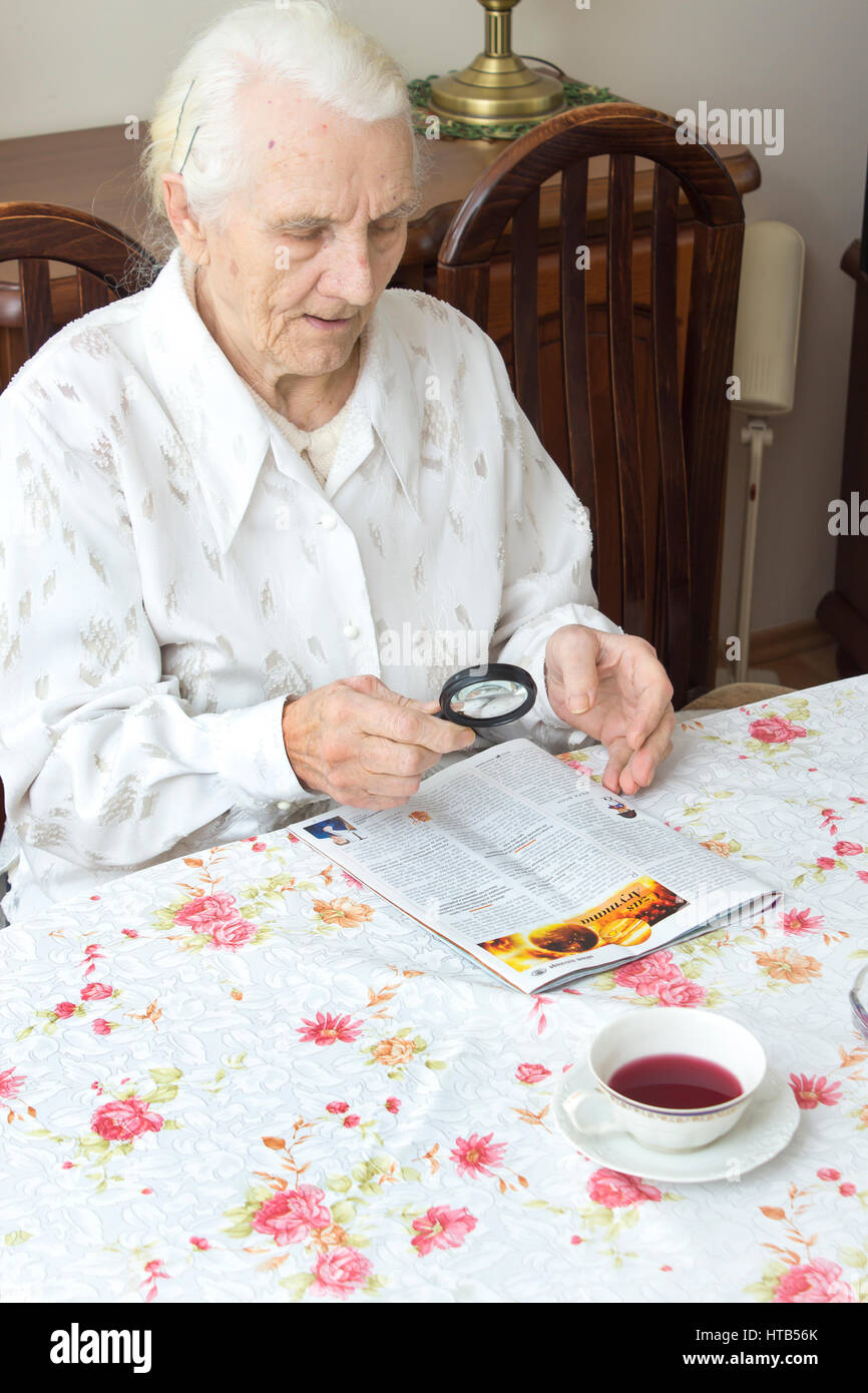 The old woman sits at a table with a newspaper. Grandmother reading a  newspaper holding a magnifying glass. Grandma reads a newspaper article  with a m Stock Photo - Alamy