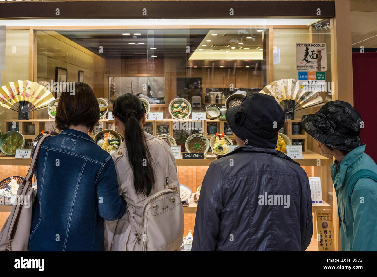 Four female, women, looking at fake food menu through the window of a  Japanese restaurant, Kyoto, Japan Stock Photo