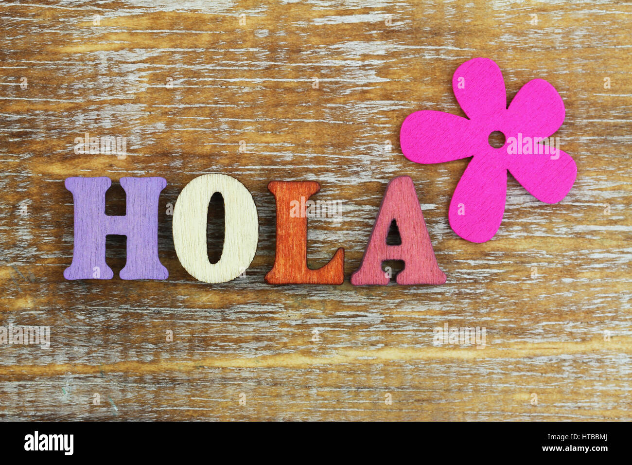 Hola (hello in Spanish) written with colorful wooden letters and pink flower Stock Photo