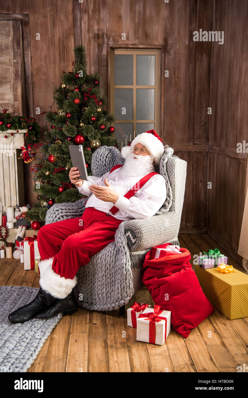 Santa Claus sitting in armchair using digital tablet an pointing Stock ...