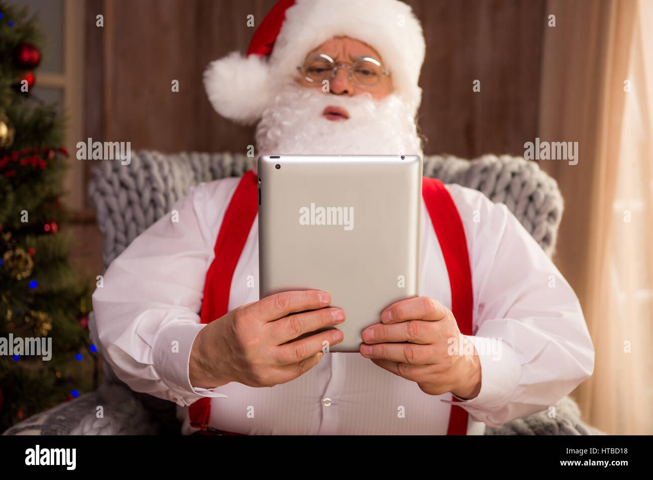 Portrait of Santa Claus sitting in armchair and using digital tablet ...