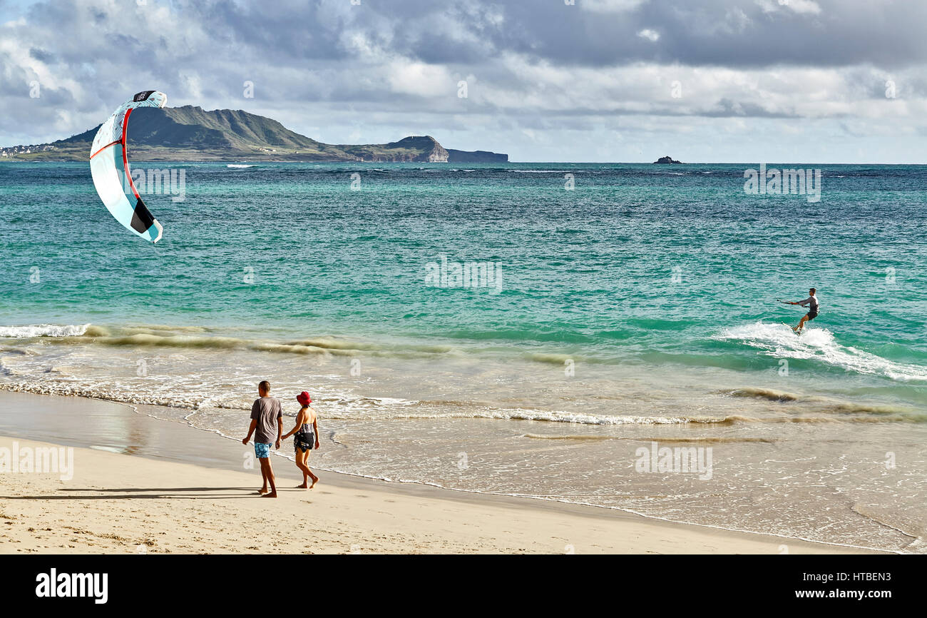 Kailua, Hawaii, USA - July 30, 2016: A man kitesurfs in the early morning while people walk by on the beach at Kailua Bay in Hawaii Stock Photo