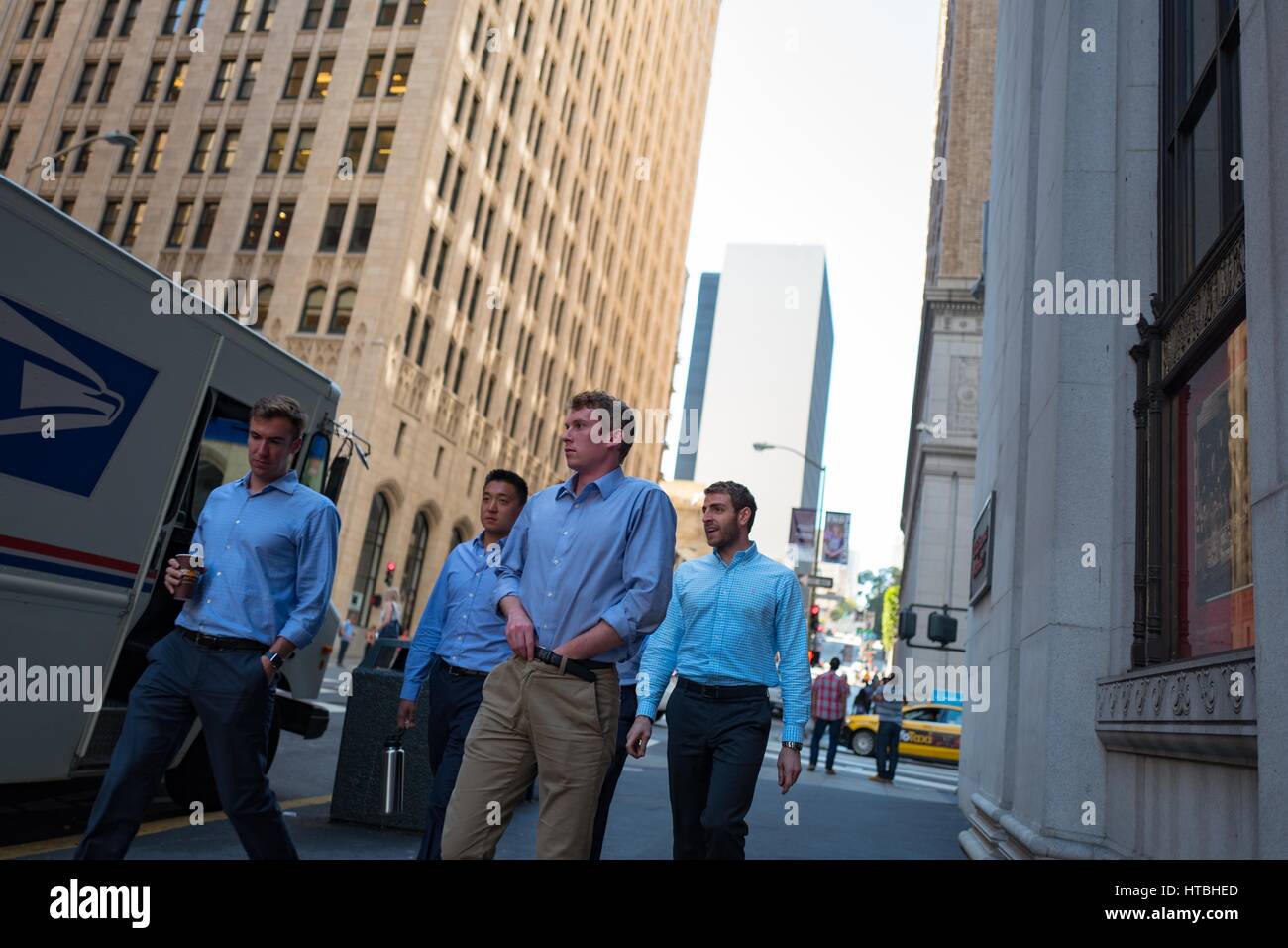 Four young men, possibly bankers, wearing identical blue button down shirts walk past a building in the Financial District neighborhood of San Francisco, California, with one man holding a cup of coffee, September 26, 2016. Stock Photo