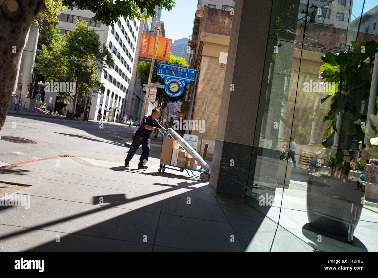 In the Financial District neighborhood of San Francisco, California, a Fedex delivery person pushes a cart loaded with parcels towards the entrance of a glass walled office building, September 26, 2016. Stock Photo