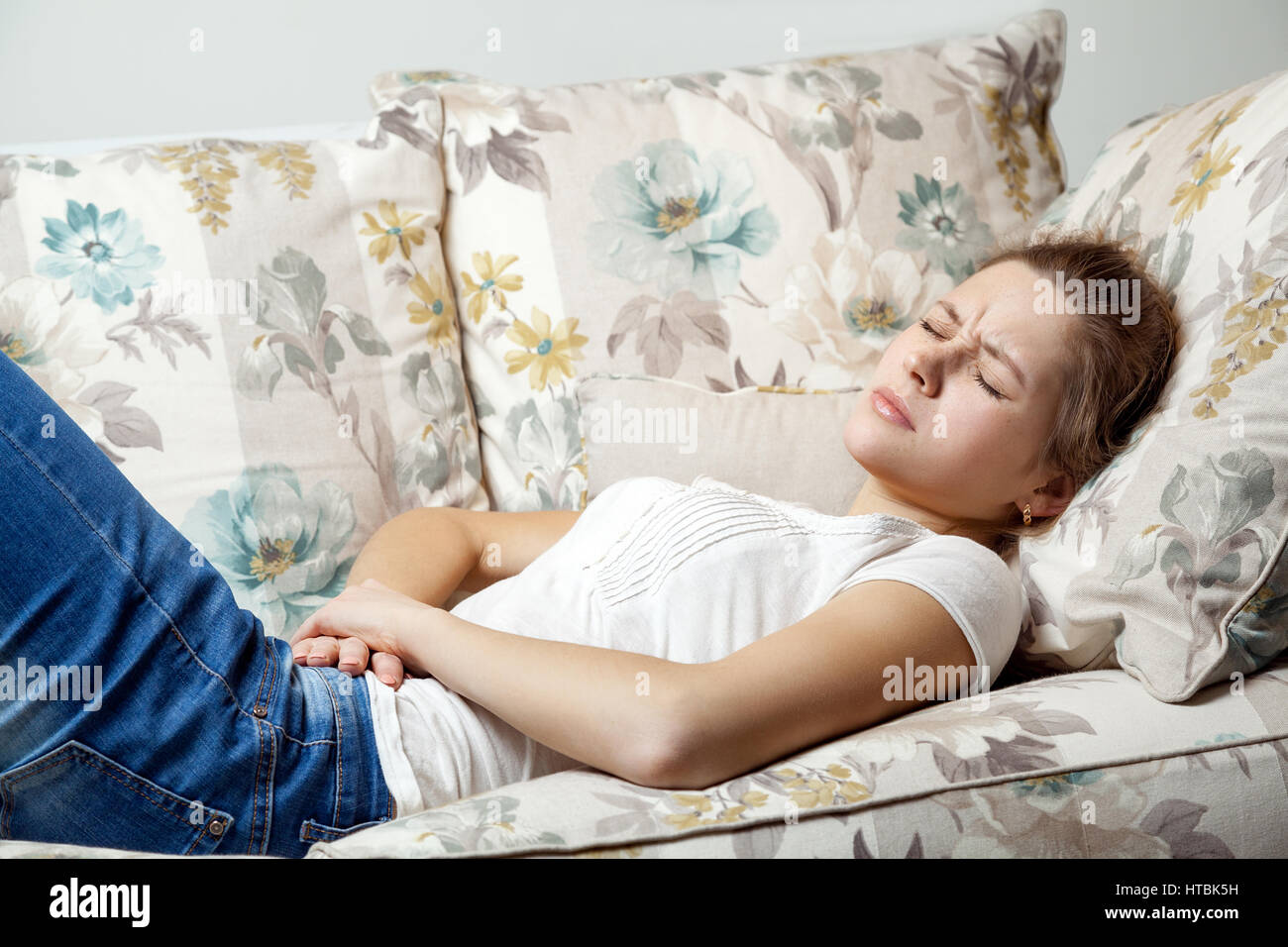 Young beautiful girl with stomach pain lying on the sofa. Stock Photo