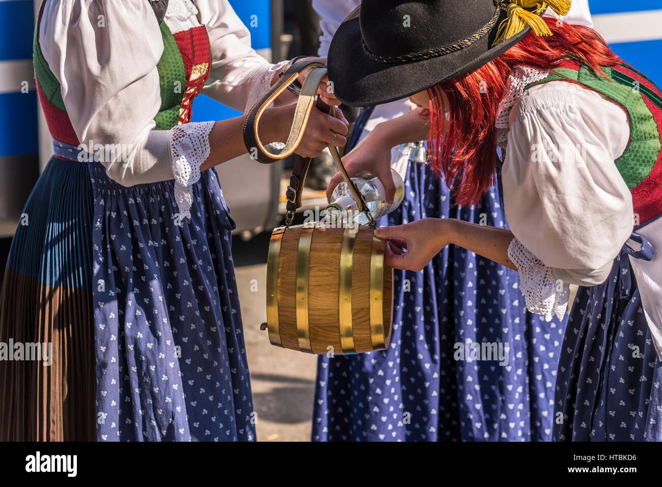An Austrian women with bright red hair a wearing a dirndl pours Schnapps into a small keg with shoulder strap in Vienna. Stock Photo