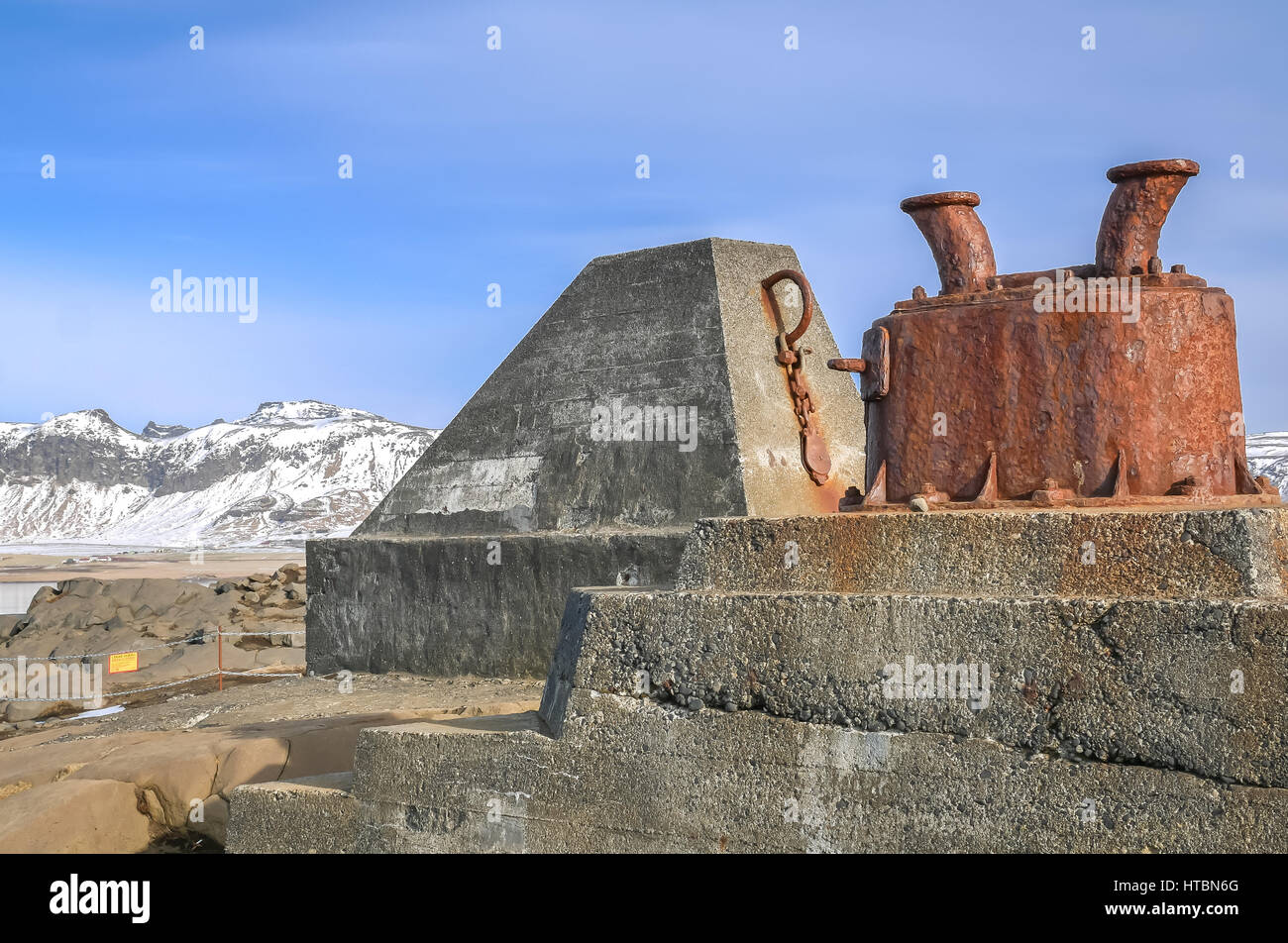 Close up of mooring cleat post on coastline at Dyrholaey, Iceland, in winter with blue sky and snow covered mountains in distance Stock Photo