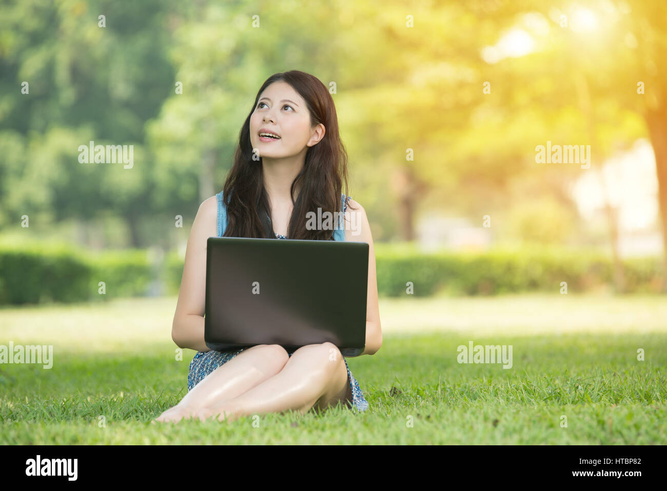 beautiful asian woman using computer sitting on grass in outdoor park ...