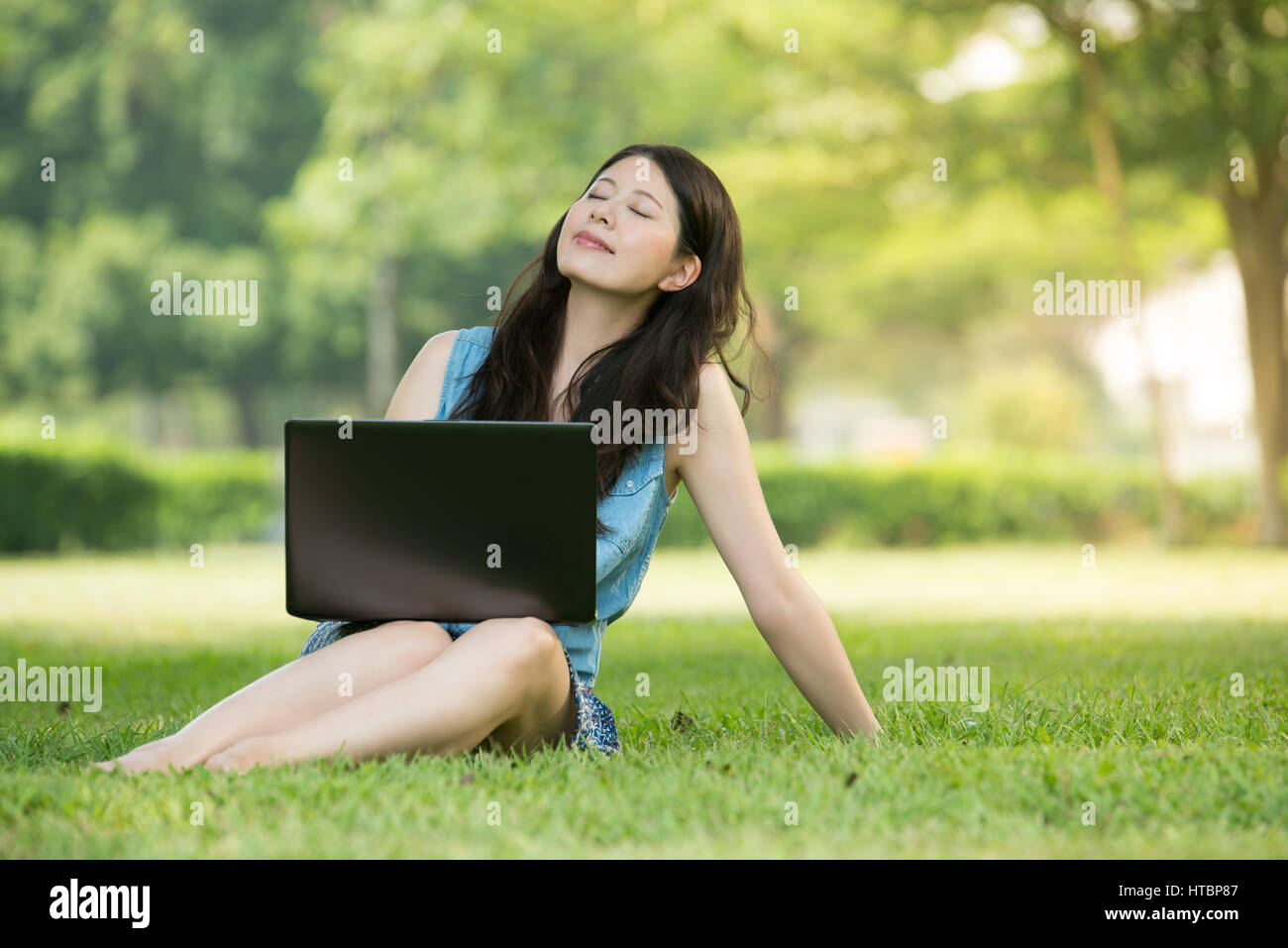 beautiful asian woman using computer sitting on grass in outdoor park ...