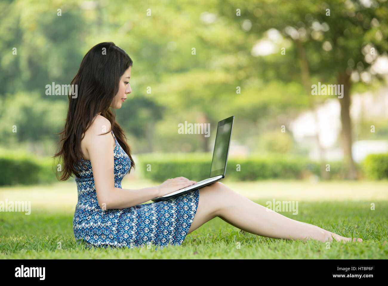 beautiful asian woman using computer sitting on grass in outdoor park ...