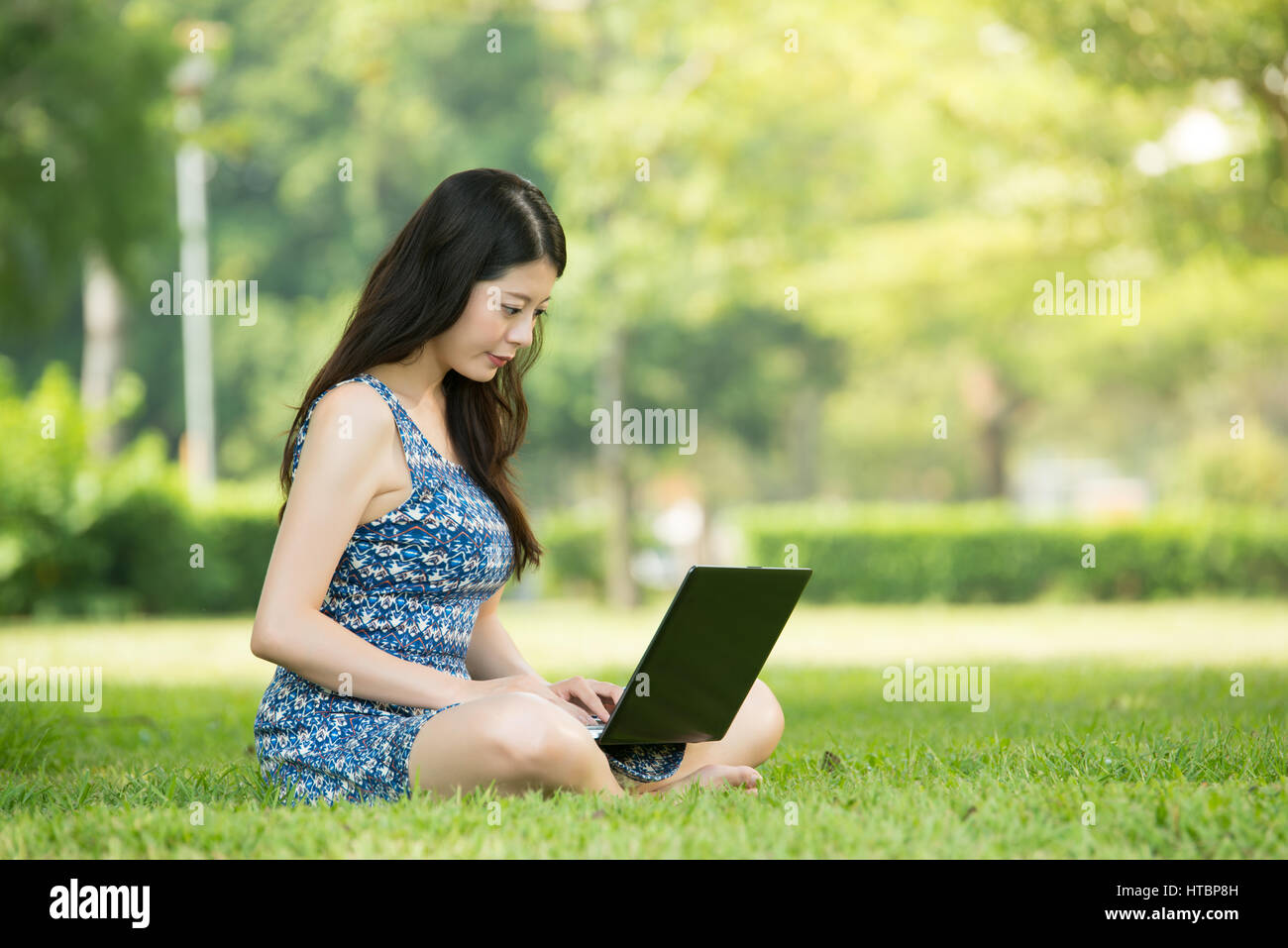 beautiful asian woman using computer sitting on grass in outdoor park ...