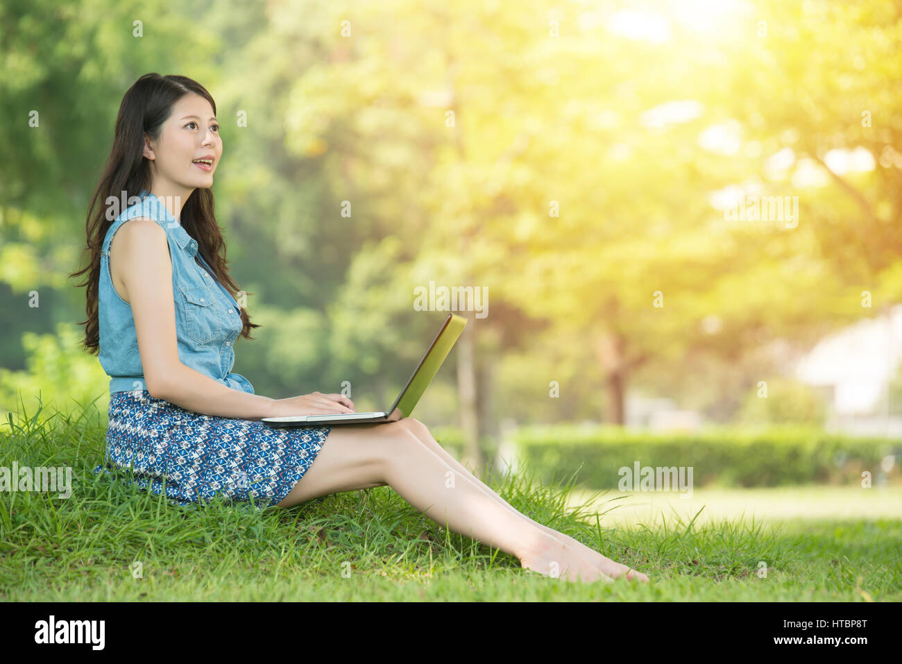 beautiful asian woman using computer sitting on grass in outdoor park ...