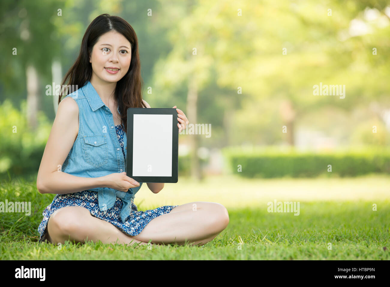 beauty asian woman presenting digital tablet sitting on grass in ...
