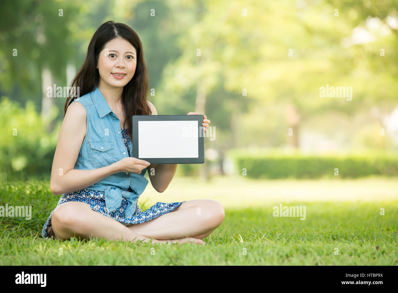 beauty asian woman presenting digital tablet sitting on grass in ...