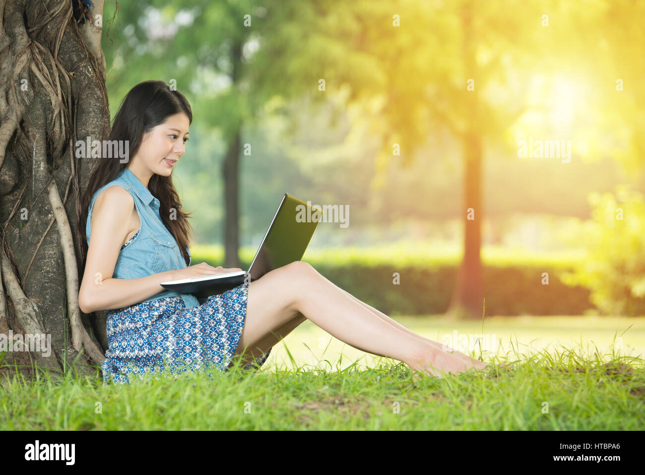 beautiful asian woman using computer sitting on grass in outdoor park ...