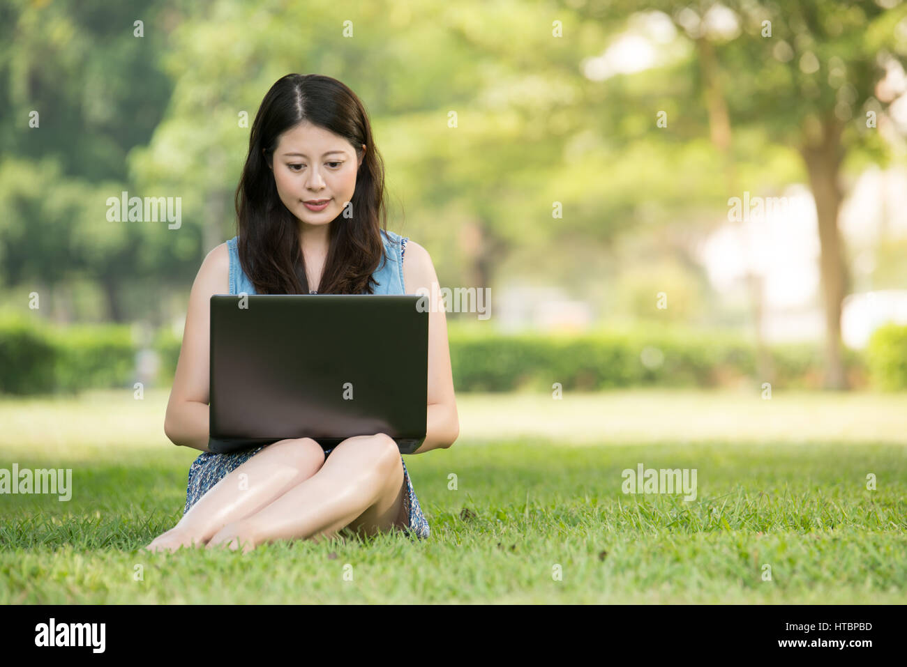 beautiful asian woman using computer sitting on grass in outdoor park ...