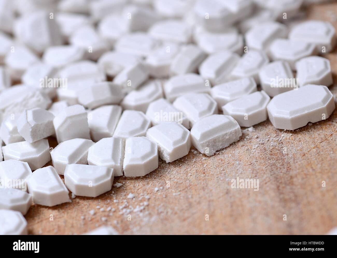 Macro of the white pills cut into pieces on wooden brown background. Stock Photo