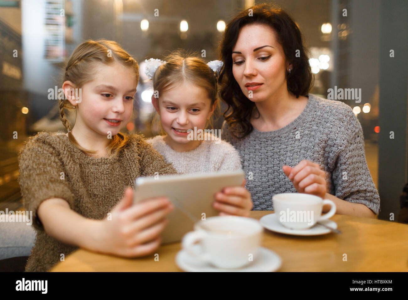 Twins and young woman looking at screen of touchpad by table in cafe Stock Photo