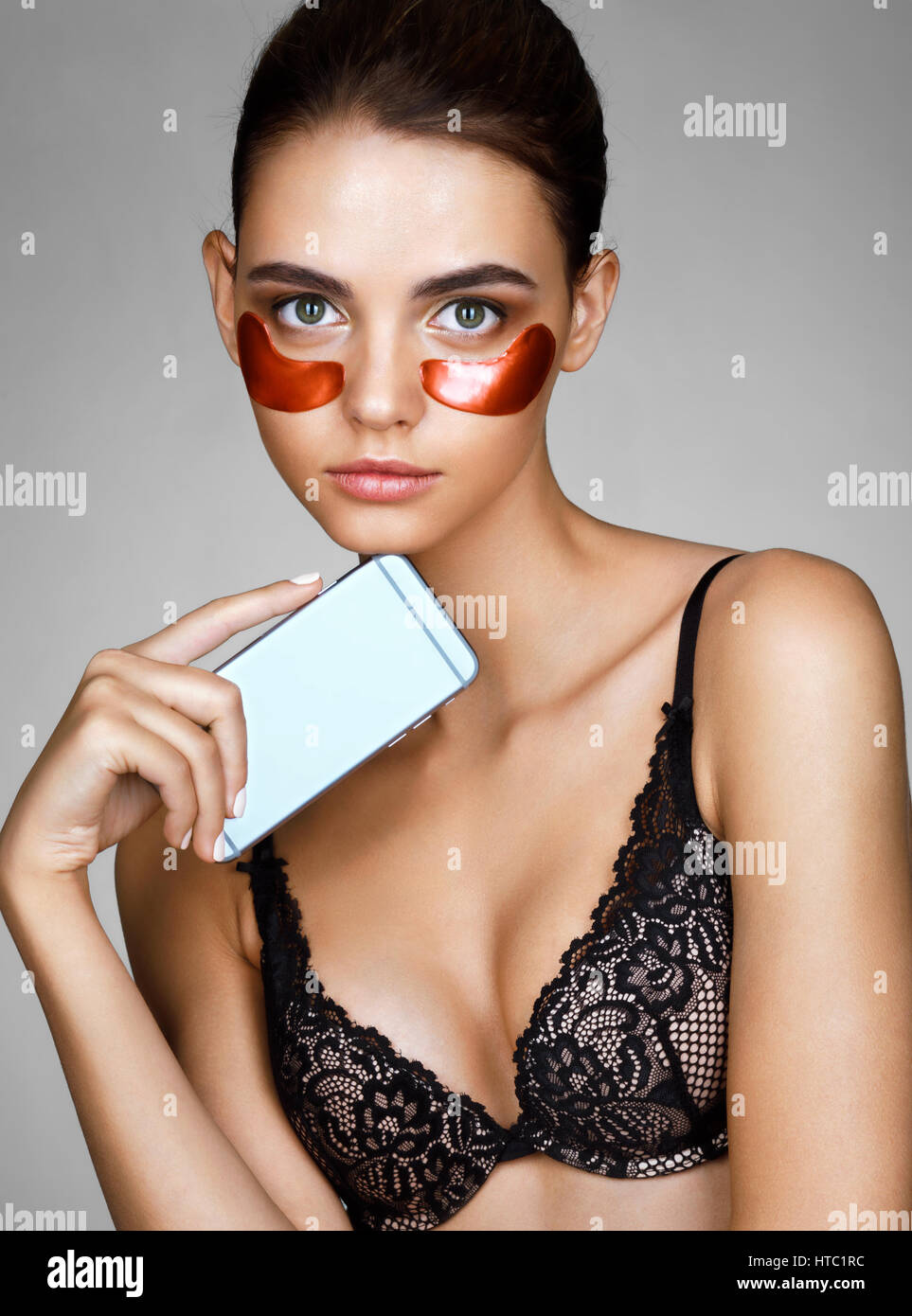 Young woman with red eyes patches and phone in hand looks at the camera. Portrait of beautiful woman with perfect skin. Skin care concept Stock Photo