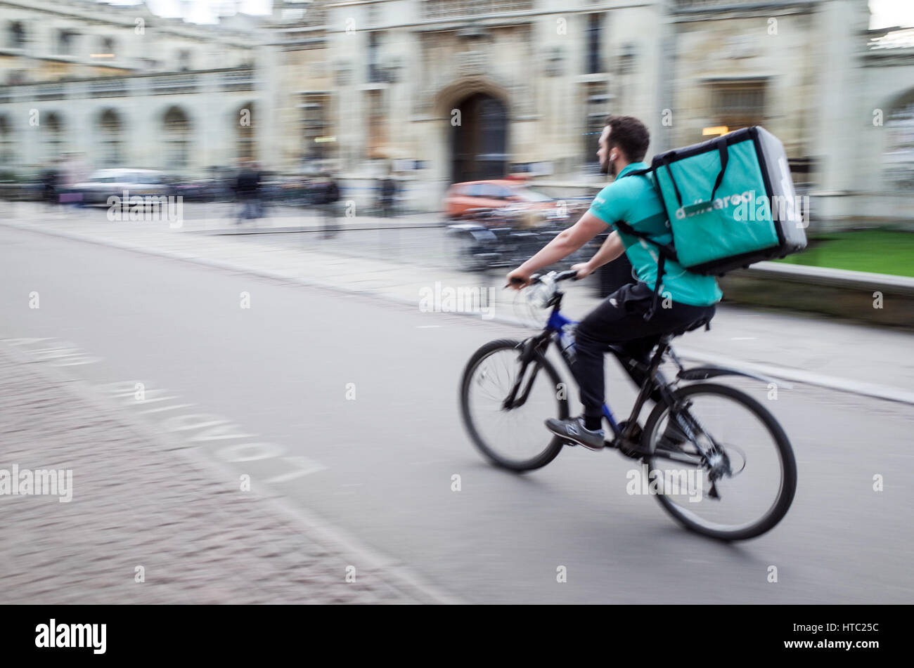A Deliveroo food courier dashes through Central Cambridge UK (Motion Blur) Stock Photo
