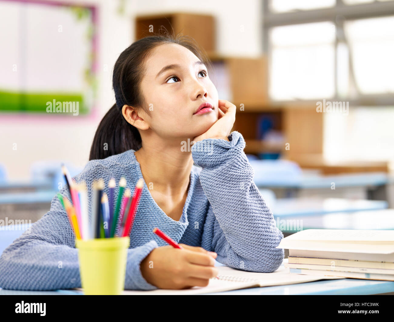 asian elementary schoolgirl looking up and thinking while studying in classroom. Stock Photo