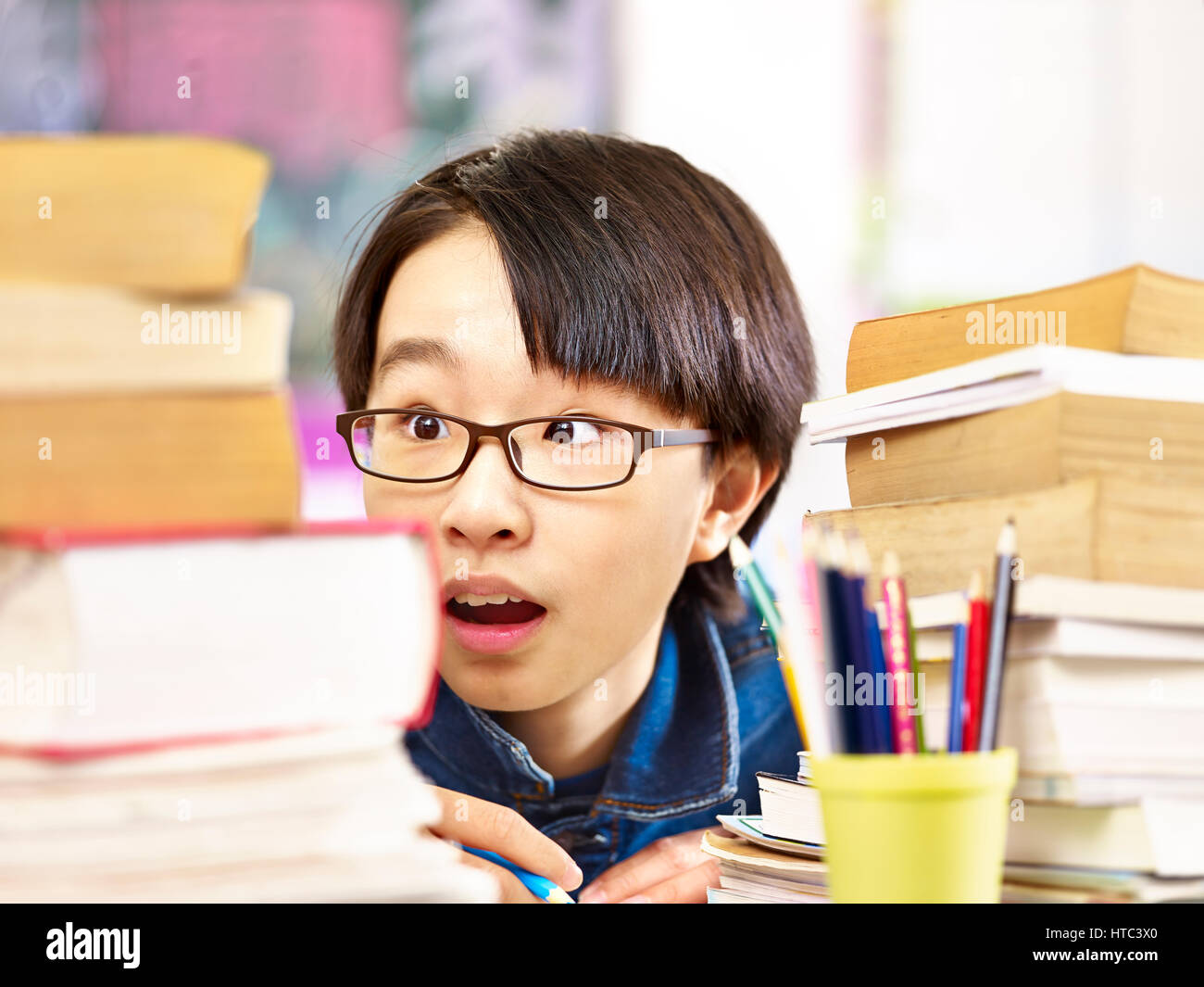 asian pupil wearing glasses appears to be shocked by the books he has to read. Stock Photo