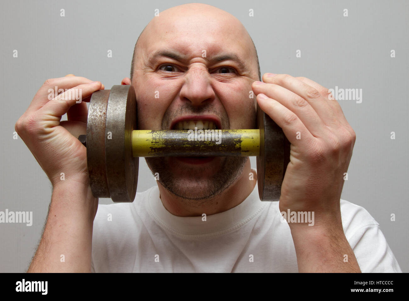 man bites his teeth into an iron dumbbell Stock Photo Alamy