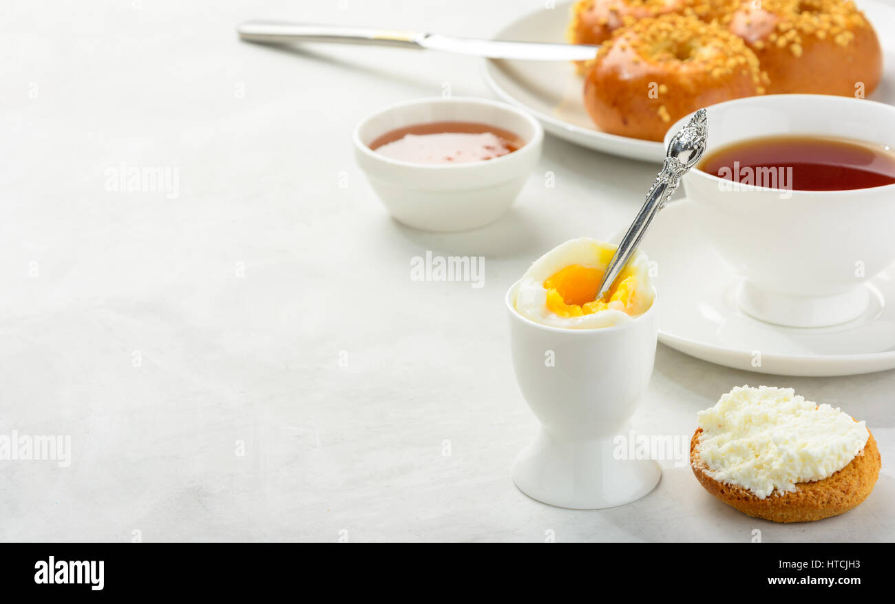 Delicious and healthy breakfast of boiled egg and brioche buns with black tea on a light background. Copy space, soft focus. Stock Photo