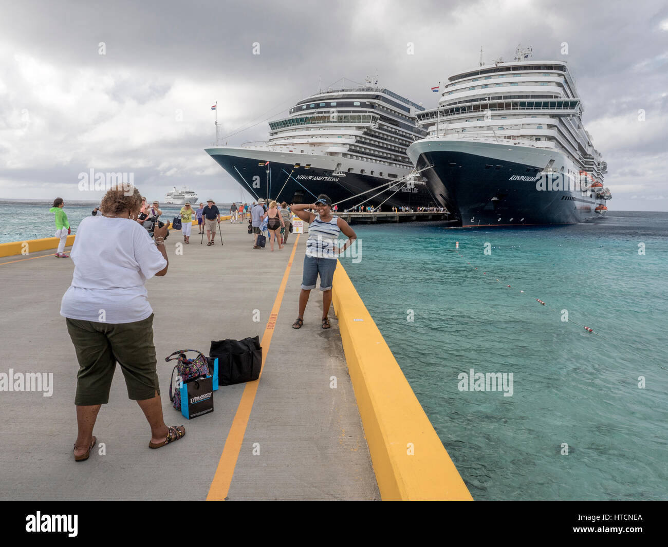 An African American Woman Takes A Photograph Of Her Friend Posing In Front Of Holland America Cruise Ships In Grand Turk Stock Photo